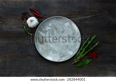 Herbs and spices around old plate on dark wooden background, top view, place for text