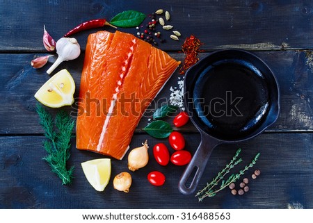 Fish salmon on dark wooden background. Fish with aromatic herbs, spices and vegetables - healthy food, diet or cooking concept