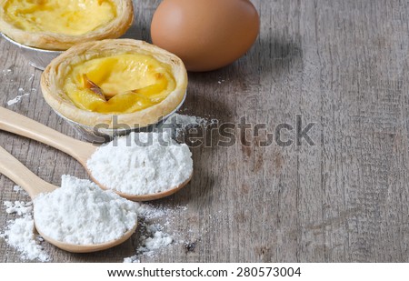 Egg tart with wheat flour in spoon and egg on wooden background.