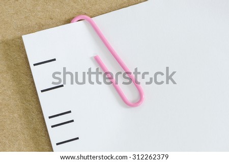 White paper with pink paper clip   on brown paper background.