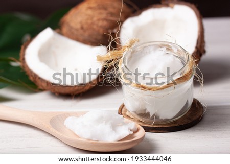 Still life of two coconuts, one of them cut in half, with a jar of coconut oil and a wooden spoon