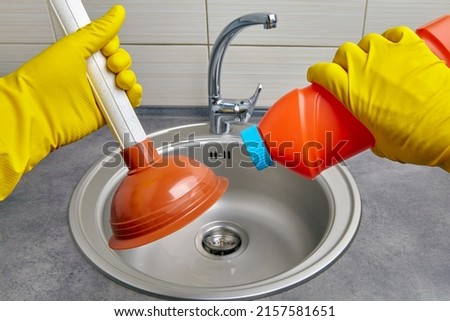 Hands in yellow rubber gloves hold a plunger and a pipe cleaner against the background of a kitchen sink. Housework cleaning a clogged sewer drain Foto stock © 