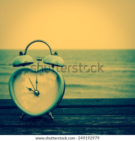 retro clock on wooden floor and blue sea, summer time on the beach vintage color tone.