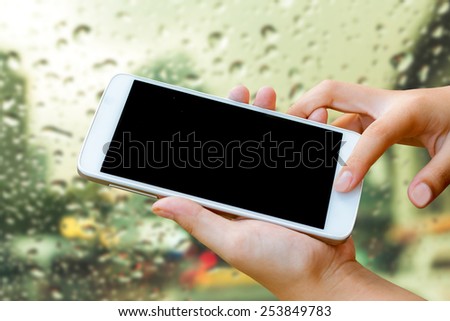 woman hand hold and  touch screen smart phone, tablet,cellphone on abstract blurred rain drop on glass in city background.