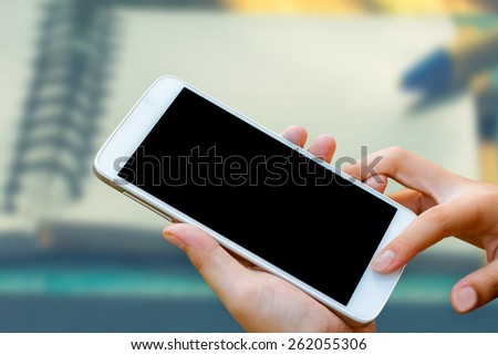 woman hand hold and touch screen smart phone, tablet,cellphone on blurred note book background.