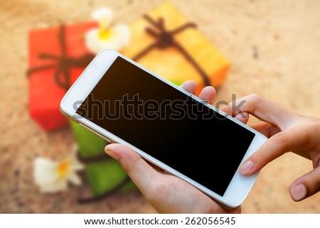 woman hand hold and touch screen smart phone, tablet,cellphone on gift box on sand beach background.