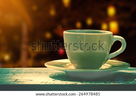 white cup of coffee or tea on wooden table over blurred of city bokeh night light background.