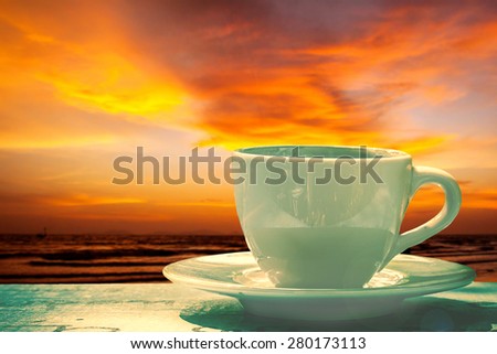 cup of coffee on wooden table over sunset beach background with sun light.