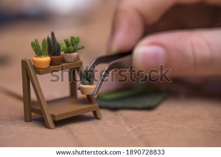 A man holds a small flower pot with tweezers. Roomboxes and miniatures. Сток-фото © 