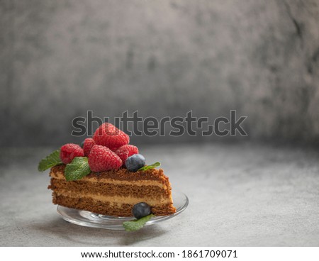 A pice of cake with raspberries and blueberries in transparent plate on a gray background with copy space. Photo stock © 