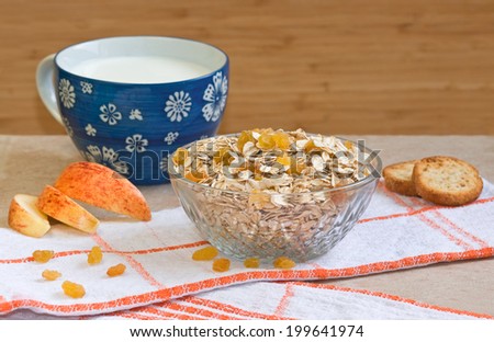 Bowl of oatmeal with raisins, blue cup of milk, slices of apple and bread on a wooden background. Selective focus.