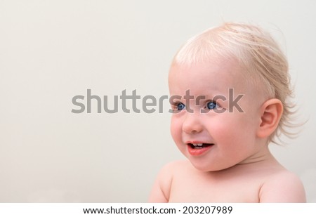 Closeup portrait of a cute smiling blond baby with blue eyes looking up on a light background