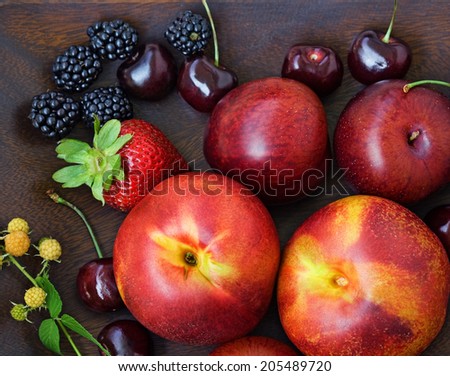 Closeup still life of ripe plums and peaches, nectarines, sweet cherry, black blackberry, red strawberry and unripe raspberry with green leaves and stalk on wooden dish, summer autumn fall harvest