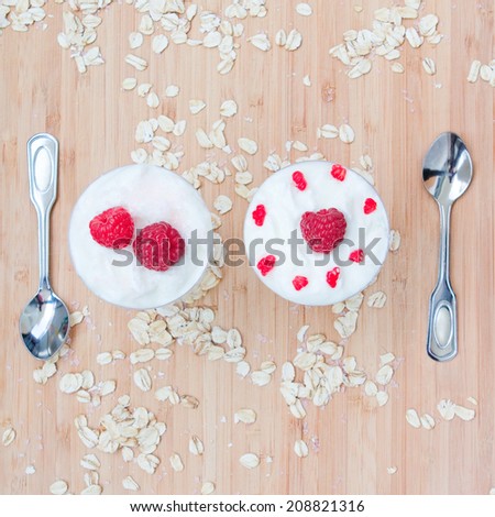 Tasty dessert meal breakfast of raspberries with cream and oatmeal on a light wooden background with silver spoons