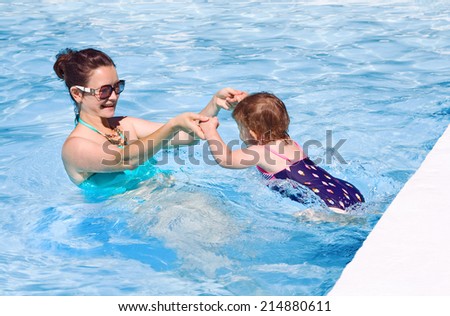 Mother and daughter playing in water in swimming pool on sunny summer day, training to swim, healthy lifestyle