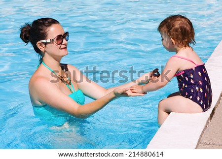 Mother and daughter playing in water in swimming pool on sunny summer day, training to swim, healthy lifestyle