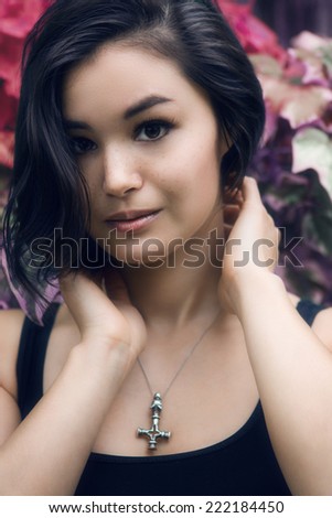 Closeup portrait of a beautiful young Asian Japanese girl woman with freckles, with black short haircut looking into the camera in garden with flowers
