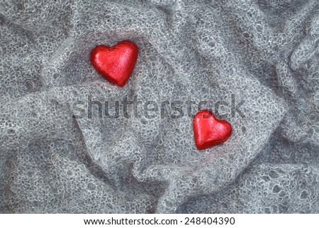 Closeup macro texture of grey knitted wool fabric material shawl scarf with red candy hearts on top, clothing background with wrinkles and folds, Valentine holiday card, love concept
