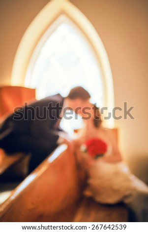 Blurry, soft, out of focus closeup portrait of smiling kissing young married couple, wedding day in church, blurry background