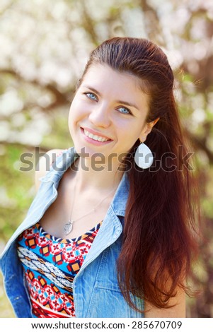 Closeup portrait of smiling beautiful sexy Caucasian adult girl woman with long dark red brown hair and blue eyes in tshirt with folk motifs and jeans vest with silver round drop earring