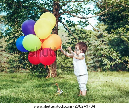 Portrait of cute adorable little asian girl child, one years old, in white clothes with balloons on field meadow back lit with sunset, concept of happy birthday holiday, toned with Instagram filters