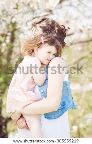 Portrait of caucasian pregnant mother in long white dress and jeans jacket holding her daughter in pink clothes on spring summer day in park outside, caring protecting parenting concept