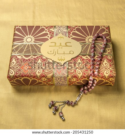 A tag with \'Eid Mubarak\' message in arabic script on a golden gift box along with islamic rosary