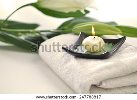 Scented candle and flowers placed on white towel - spa objects