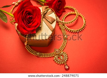 Traditional indian gold necklace and bangles set arranged with heart-shaped gift box and red rose flowers.