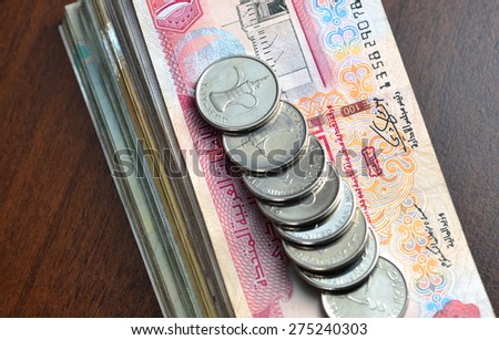 Many one dirham coins placed on stack of hundred dirham notes. Top angle.