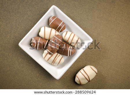 Date fruit chocolates. Top view of a white bowl with plenty of date chocolates..
