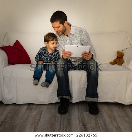 Baby and father playing with tablet on a white sofa both watching stuff of each other