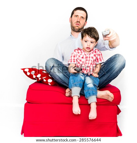 Bored father  and baby using remote control and watching tv together on a red sofa - isolated on white background
