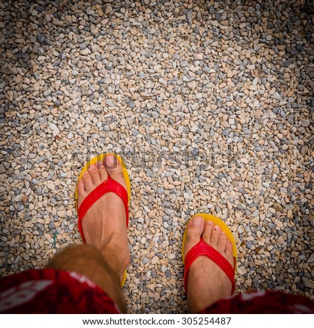 Close up of feet wearing yellow and red flip-flops on the stones
