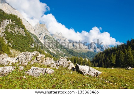 Beautiful mountain landscape. There are big stones in the foreground. Ridge goes over the horizon. There is a forest at the foot of the mountains. The sky is blue and cloud.  Nobody is around.