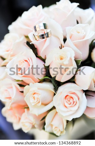 Two wedding rings lie on a bouquet of light pink roses.  Rings are golden.