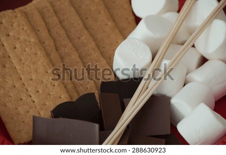 S\'more ingredients: chocolate, marshmallow, graham cracker, and sticks.