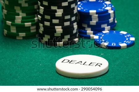 Dealer chip, and other varied poker chips, on green felt.