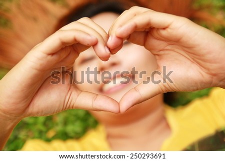 woman lies down on green grass showing hands in heart-shaped with smile mouth behind