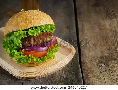 Burger with beef cutlet, lettuce, onions and tomato in bun with sesame seed. Space for text