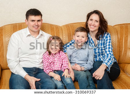 Happy parents, their daughter and the son sit on a sofa.