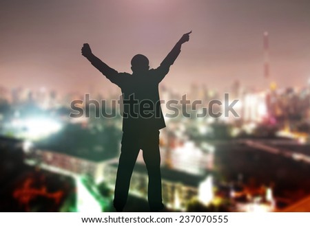 Silhouette businessman raising hands with pen and phone over blurred city at night background.