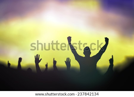 Silhouette people raising hands over blurred stadium.