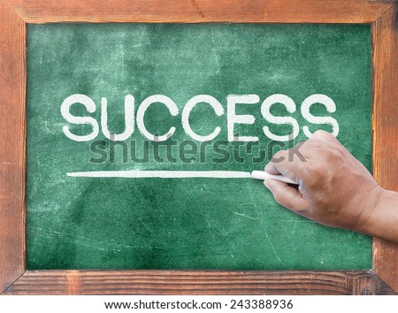 Human hand holding chalk and writing text for SUCCESS on green board.