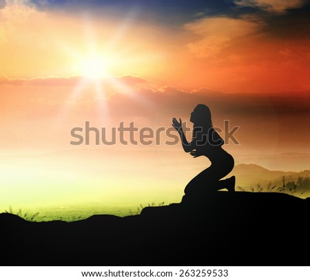Silhouette of woman kneeling and praying over beautiful sunset background.