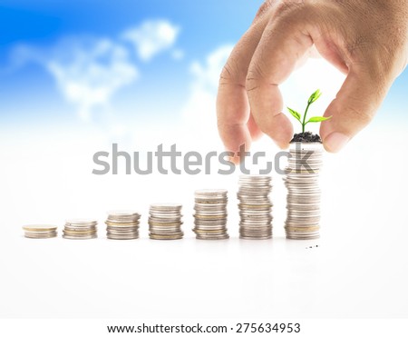 Human hand adding a coin with young plant in the final row over blurred world map of clouds background. Money coin concept.