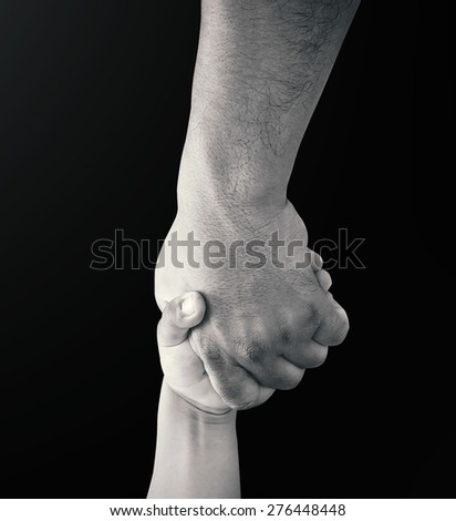 Father hand holding child hand over black background.