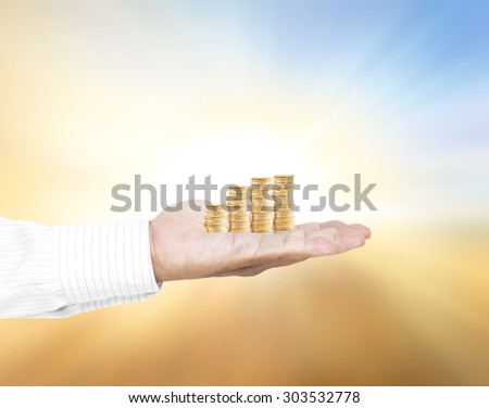A handful of golden coins in the palm of a hand over blurred beautiful sunset background. Money coin concept.