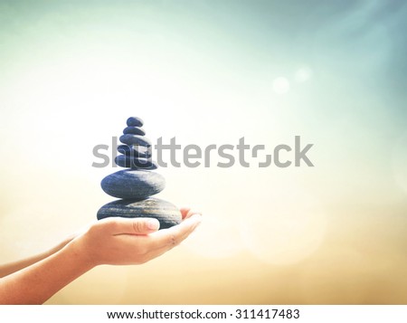 Human hands holding balanced seven Zen stones over blurred beautiful nature background. Ecology, Sustainability concept.