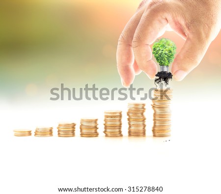 Human hand adding light bulb of tree in the final row over blurred nature background. Money coin concept.
